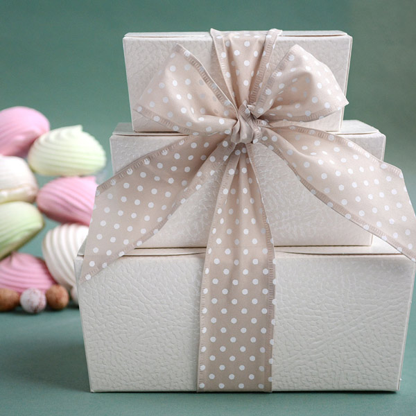3 white textured 'ballotin' boxes stacked in order of size and tied with a taupe-white polka dot ribbon