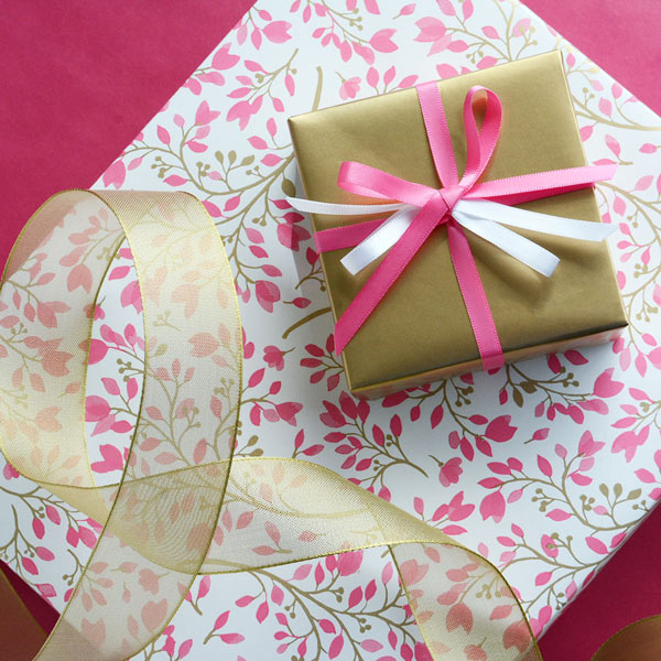 Gift wrapped in gold paper with satin ribbons, on top of gift wrapped in pink and gold floral wrap