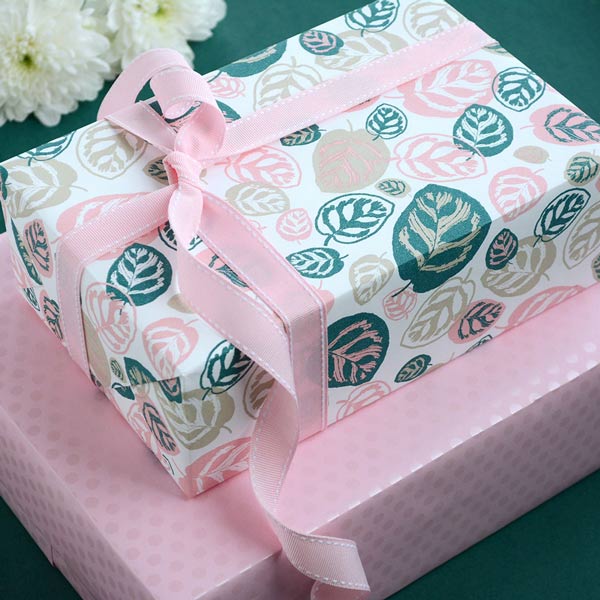 2 boxes stacked & wrapped in green, pink and stone themed wrapping paper. Finished with a pink grosgrain ribbon